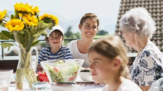 Familie mit Grosseltern essen gemeinsam draussen in der Sonne.